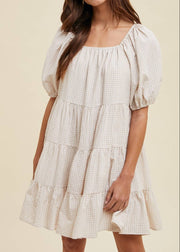 Woman wearing a checkered dress with puff sleeves on a beige background