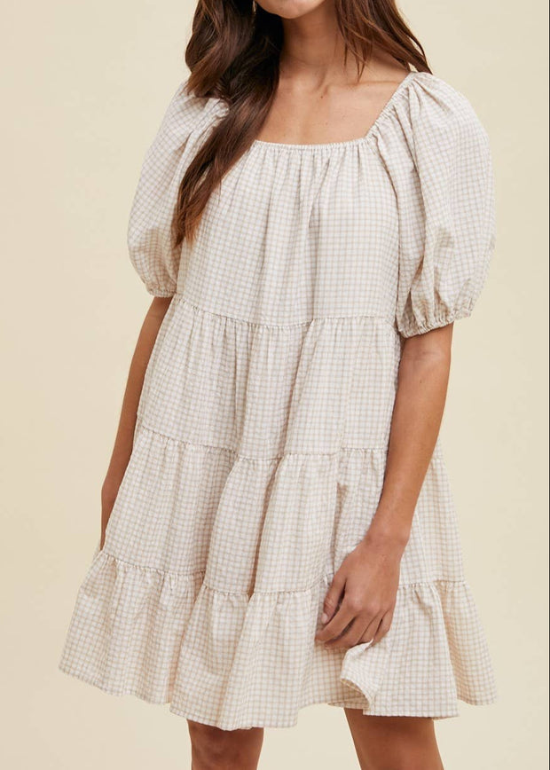 Woman wearing a checkered dress with puff sleeves on a beige background